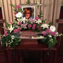 Floral funeral tribute with pink roses, white lilies, and daisies around a framed photo