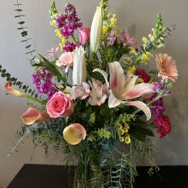 Mixed bouquet with pink roses, lilies, calla lilies, and purple blooms in a glass vase