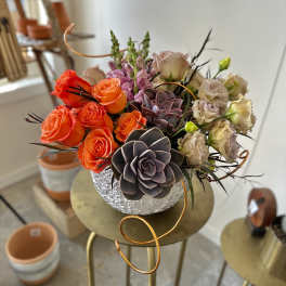 Bouquet of orange roses and beige blooms in a textured silver vase