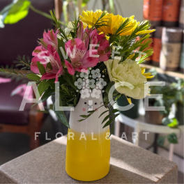 Mixed bouquet of pink, yellow, and cream flowers in a yellow and white face vase