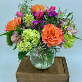 Mixed bouquet of orange roses, pink tulips, and green hydrangeas in a glass vase