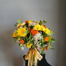 Mixed yellow and orange bouquet in a glass vase with a gold ribbon