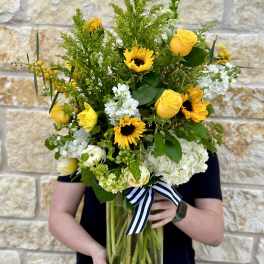 Tall bouquet of yellow roses, sunflowers, and white blooms in a glass vase