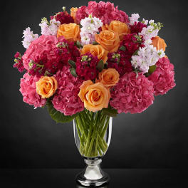 Bouquet of pink hydrangeas, orange roses, and white stock in a clear vase