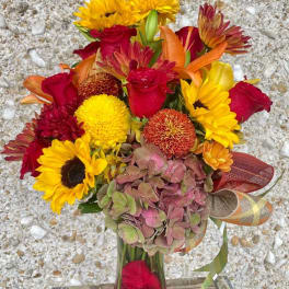 Bouquet of red roses, yellow sunflowers, and orange blooms in a glass vase