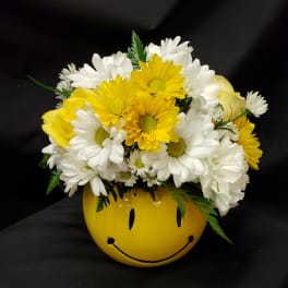 Yellow and white daisy bouquet in a smiley-face vase