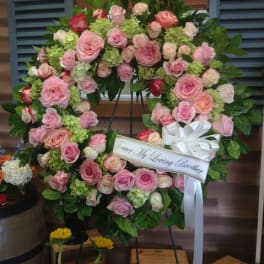 Pink rose funeral wreath with a white ribbon on a stand