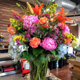 Tall mixed bouquet in a clear glass vase with lilies, roses, peonies, and hydrangeas
