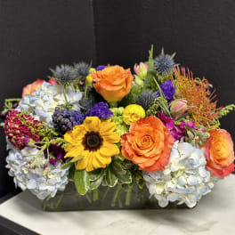 Colorful mixed flower arrangement in a rectangular glass vase