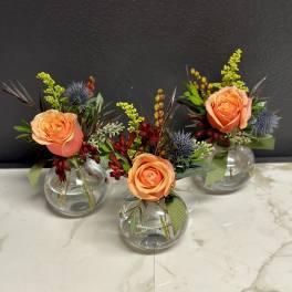 Three small floral arrangements in round glass vases with peach roses