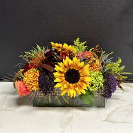 Mixed bouquet with sunflowers, roses, and chrysanthemums in a rectangular glass vase