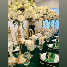 White floral centerpieces on gold stands above a green-and-gold table setting