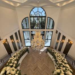 White rose arrangements line a grand staircase beneath a chandelier.