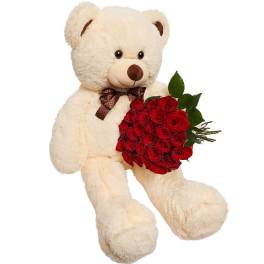 Cream teddy bear holding a bouquet of red roses