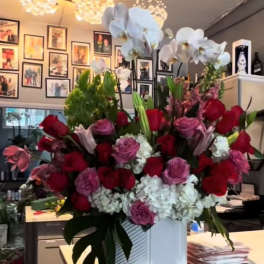Large floral arrangement with red and pink roses, white hydrangeas, and white orchids in a white vase.