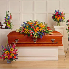 Colorful sympathy flowers with casket spray, standing sprays, wreaths, and vase around a wood casket