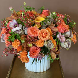 Mixed bouquet of orange, coral, and lavender flowers in a white vase