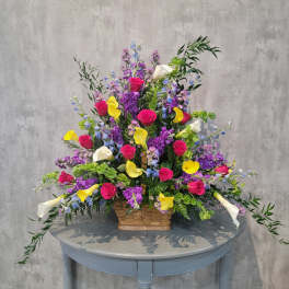 Large mixed bouquet in a wicker basket with pink roses, yellow callas, and purple flowers
