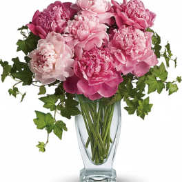 Pink peonies in a clear glass vase with trailing ivy