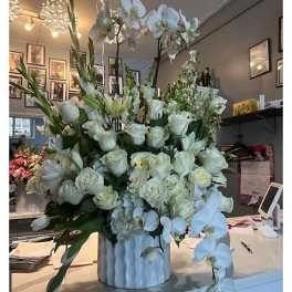 Large white floral arrangement in a white vase with orchids and roses