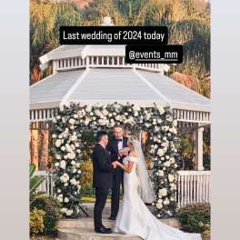 Bride and groom under a white floral wedding arch at an outdoor gazebo