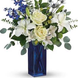 White lilies and roses in a blue glass vase with blue flowers