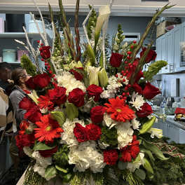 Tall red and white flower arrangement with roses, lilies, and gerbera daisies in a white ceramic vase.