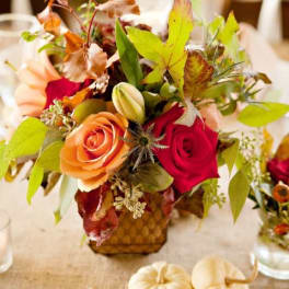 Autumn floral arrangement with red and peach roses in a small vase