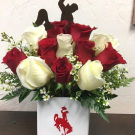 Red and white roses arranged in a white vase with a cowboy silhouette topper