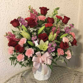 Bouquet of red roses, pink carnations, and lilies in a white vase with a pink ribbon