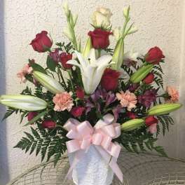 Bouquet of red roses and white lilies in a white vase with a pink ribbon