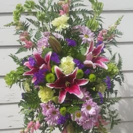Standing floral spray with pink lilies and purple daisies on an easel