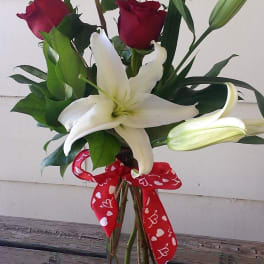 Red roses and a white lily in a glass vase with a heart ribbon
