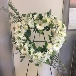 White floral wreath on a black stand with greenery accents