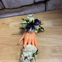 White rose wrist corsage with purple ribbon on a mannequin hand