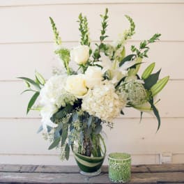 White floral arrangement in a glass vase with a green mosaic candle holder beside it