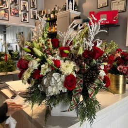 Large holiday floral arrangement with red roses and white blooms in a white container