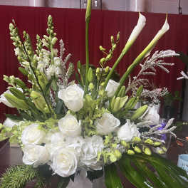 White roses and calla lilies in a white vase with green accents