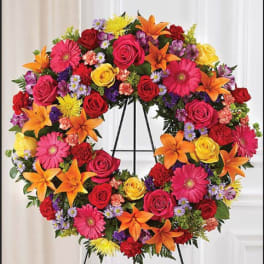 Colorful floral wreath on a black stand with roses, lilies, and daisies
