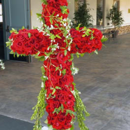 Large cross-shaped arrangement of red roses with trailing greenery