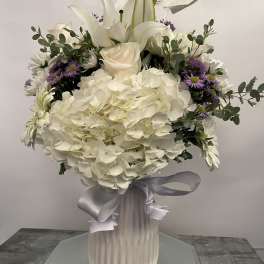 White floral arrangement in a ribbed vase with a silver ribbon