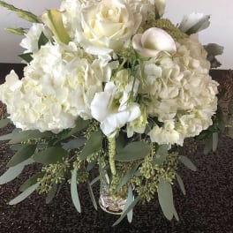 White floral arrangement with roses, hydrangeas, and calla lilies in a glass vase