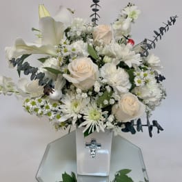 White floral arrangement in a glossy vase with a silver cross emblem