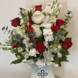 Red and white flower arrangement in a white vase with a cross emblem