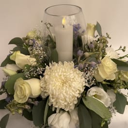 White floral arrangement around a glass candle holder with a lit candle