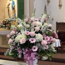 Large pink and white floral arrangement in a church with a ribboned vase
