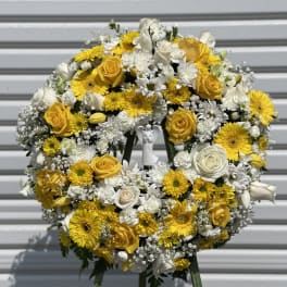 Yellow and white floral wreath on a stand with a small angel figure in the center