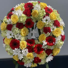 Circular floral wreath with red, yellow, and white blooms and a small cross