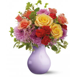 Mixed bouquet of yellow and peach roses, red carnations and purple mums in a lavender vase
