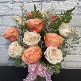 Peach and white roses in a glass vase with a pink ribbon